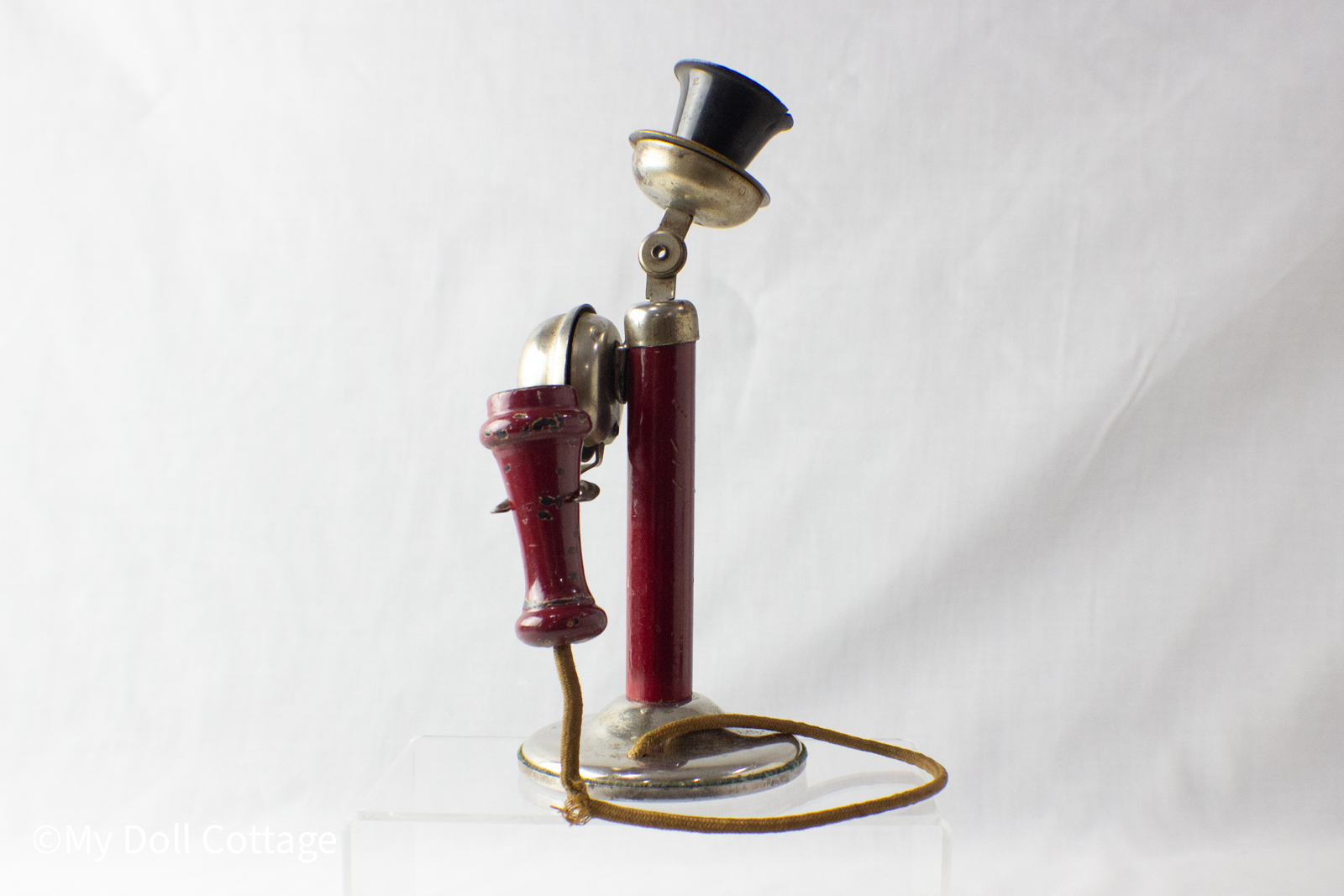 - Angled view of the toy telephone with red upright post, wooden receiver, and silver ringer attached to the side.