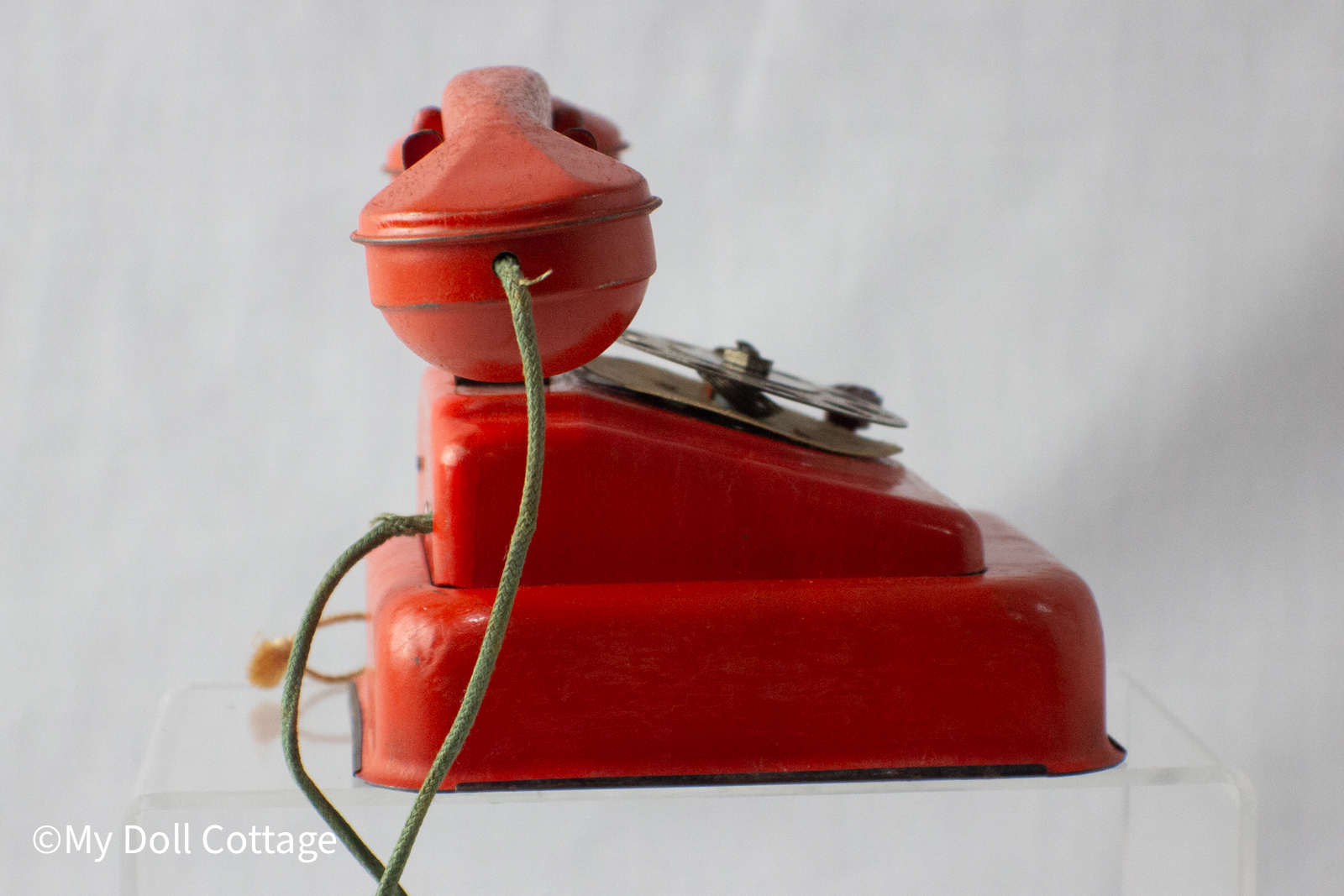 Side view left: Side profile of the red MFZ tin telephone showing green cloth cord attached to handset.