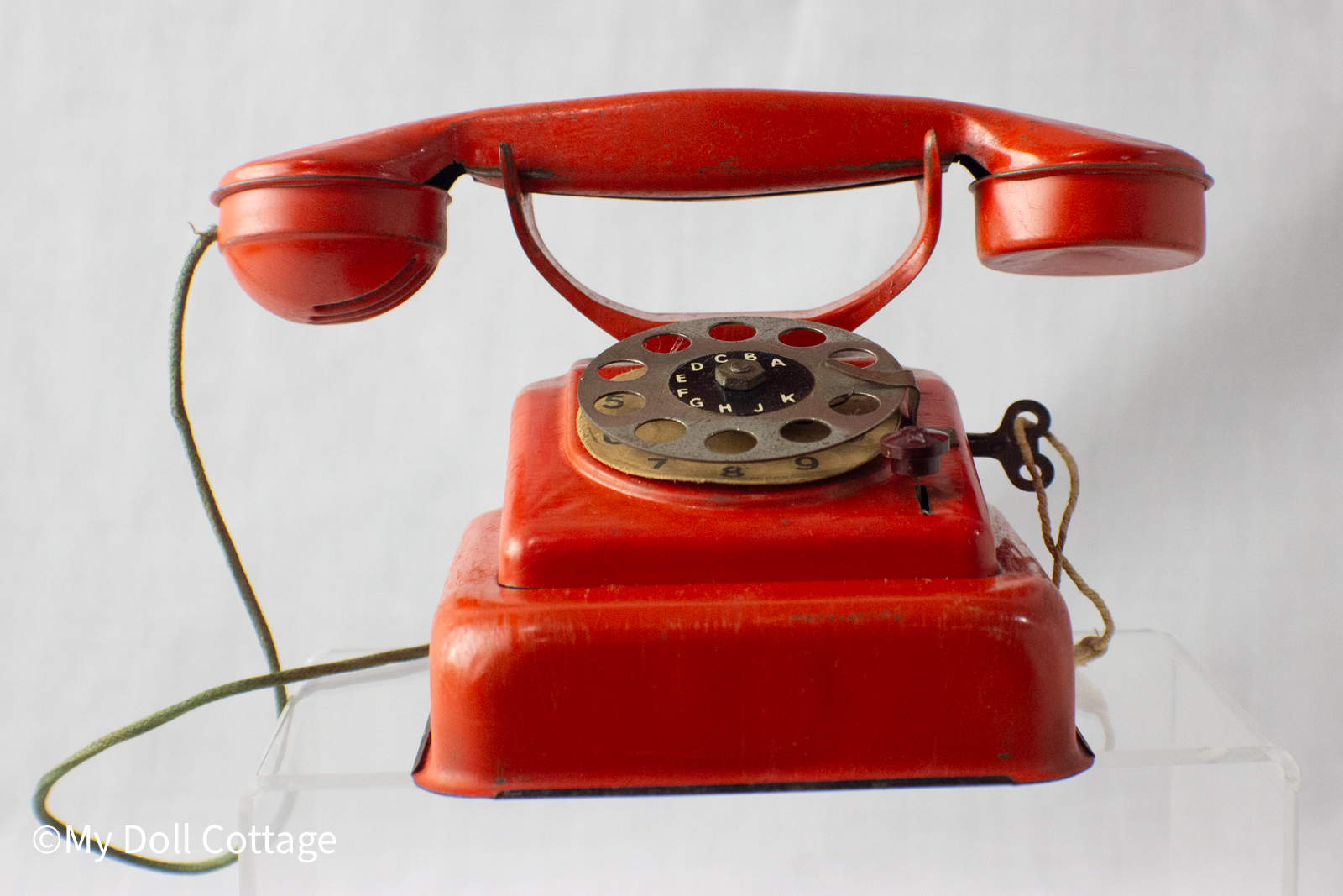 - Front view: Red 1950s MFZ tin toy telephone with tin receiver resting on cradle and metal rotary dial.