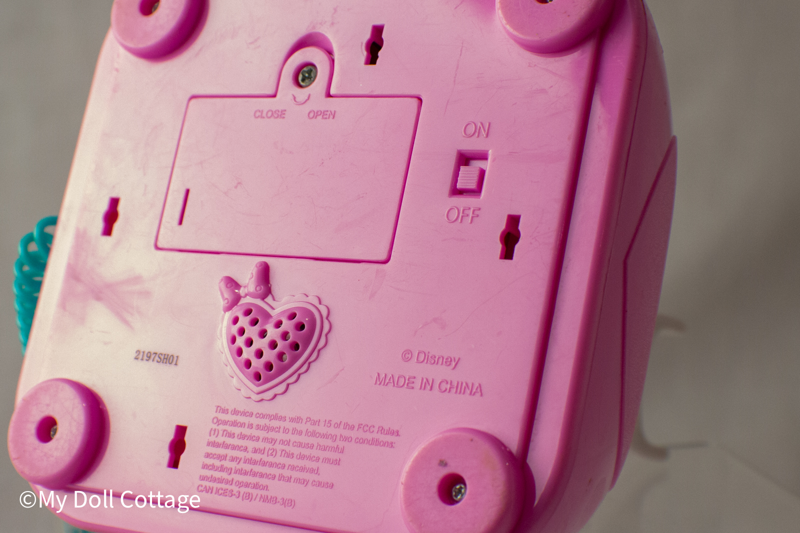 Underside of the toy phone showing battery compartment, on/off switch, speaker grill, and © Disney Made in China marking.