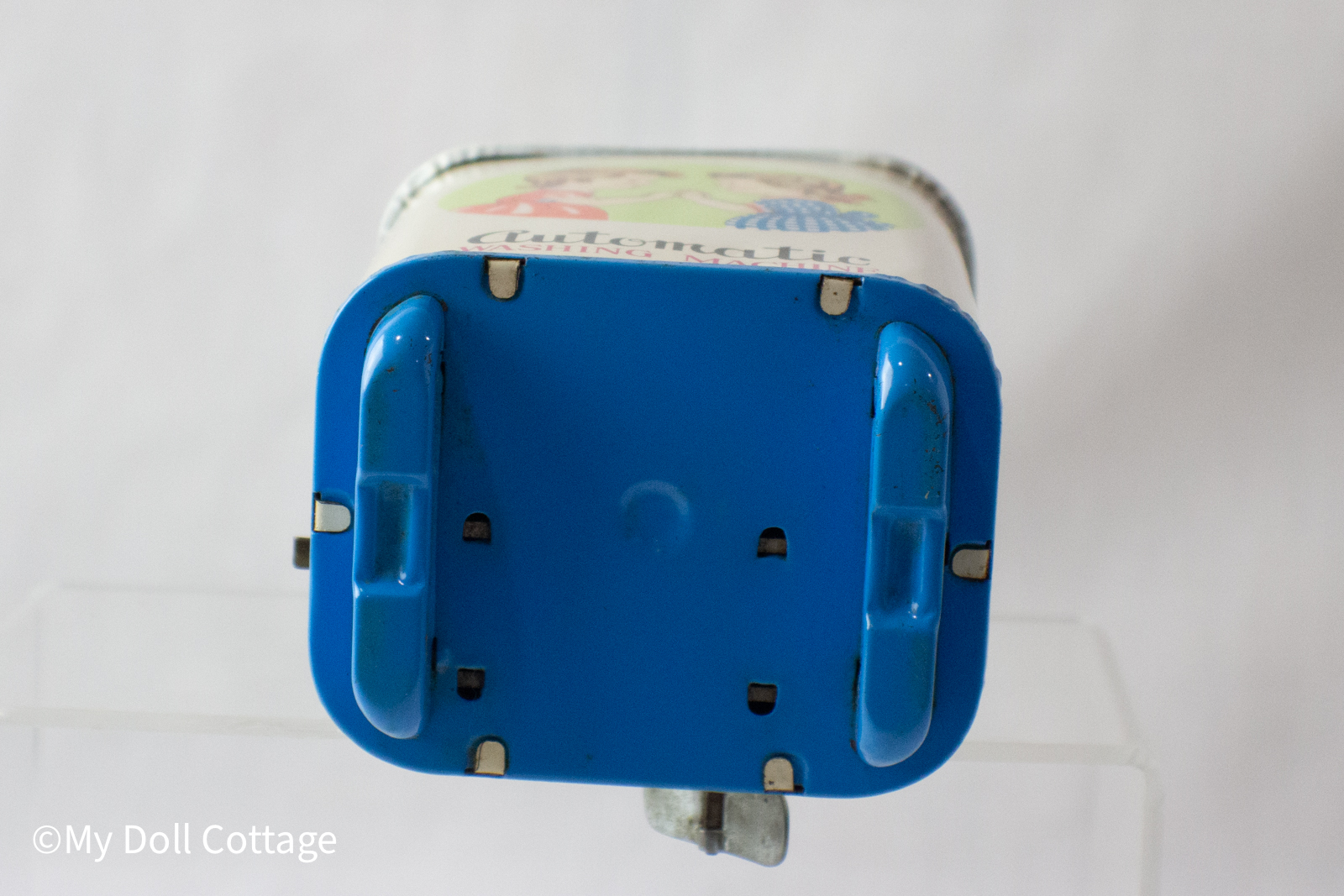 2.	Base of the tin washing machine featuring blue tin feet and structural tabs.
