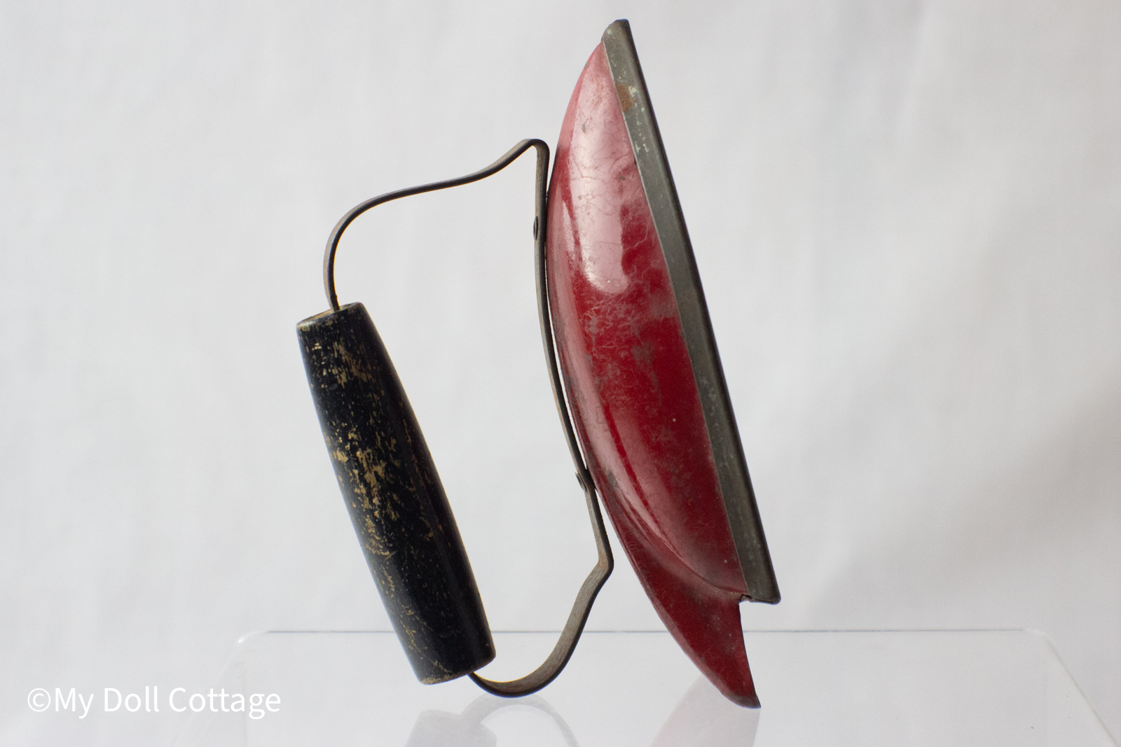 Side view of vintage red and black 1930s Wolverine Sunny Suzy toy iron with metal body and black wooden handle. 