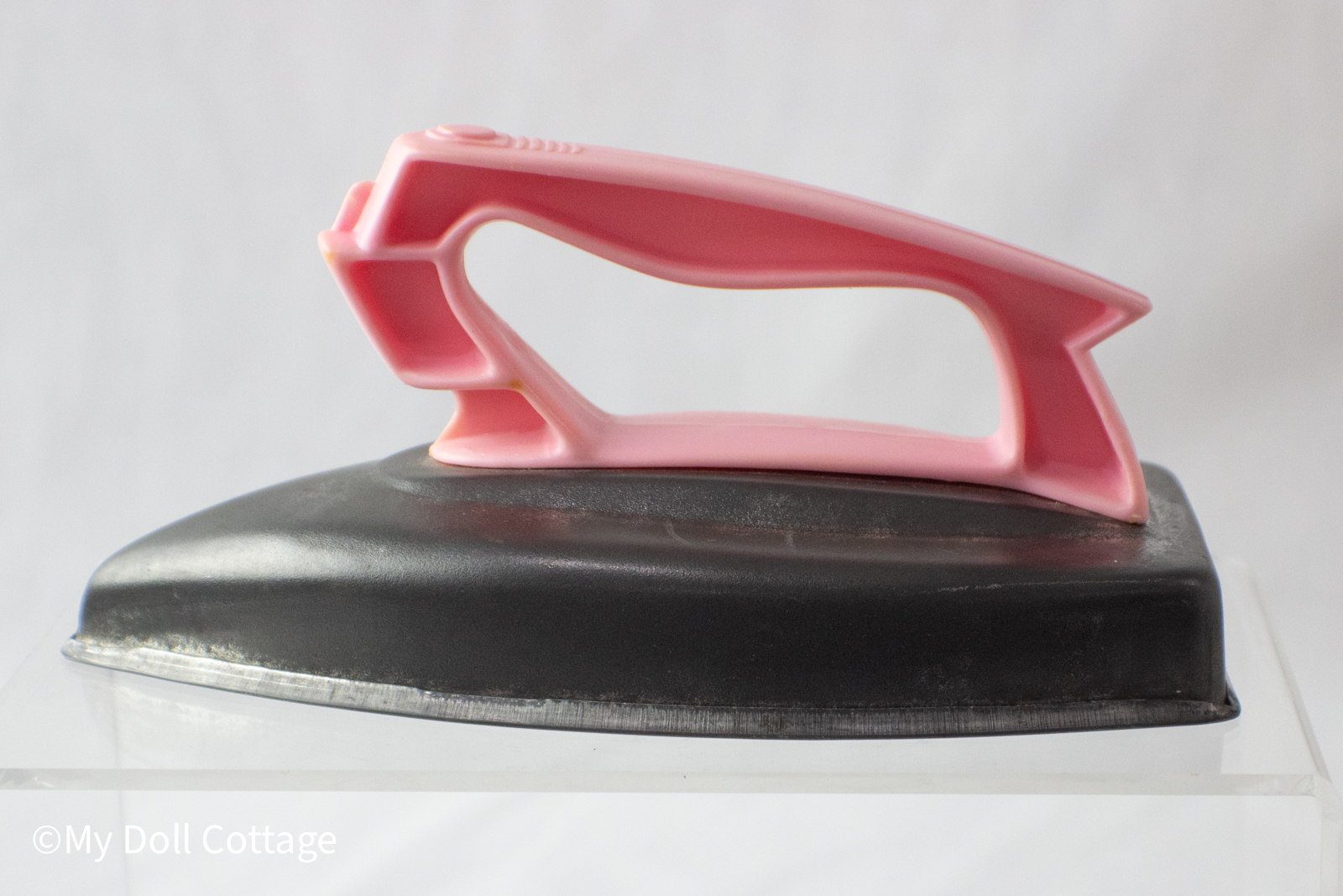 Side view of a 1950s Wolverine Toy iron showing a pink plastic handle and black pressed-metal base.