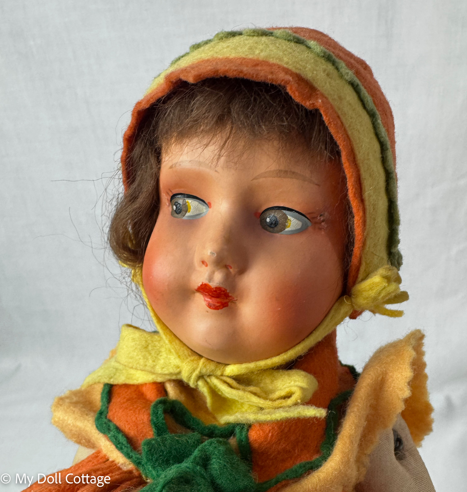 Close-up portrait of 1930s doll with painted side-glancing eyes, red lips, and original felt bonnet.