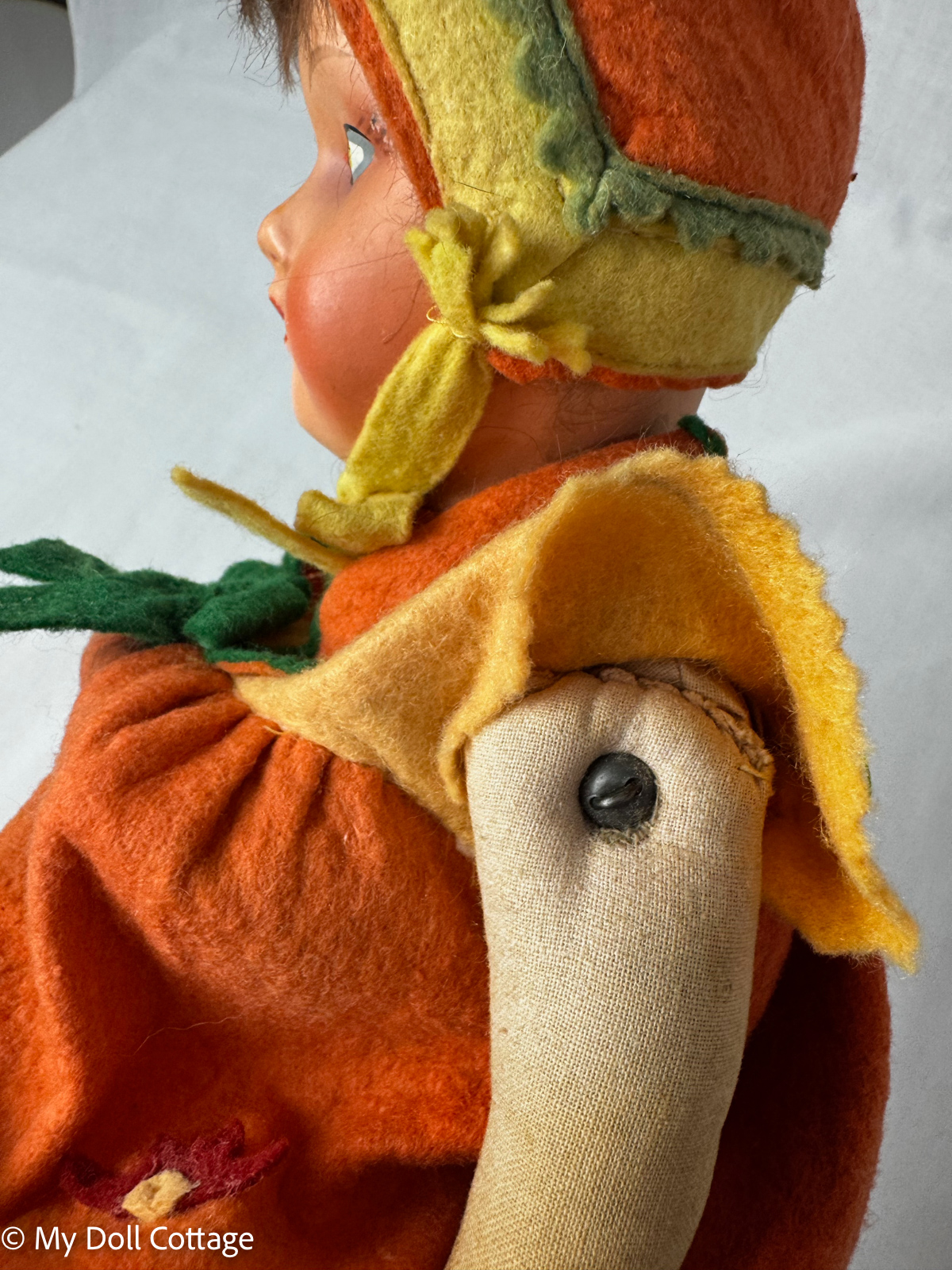 Side profile of German papier-mâché faced doll showing stitched cloth arm attachment and layered felt costume.