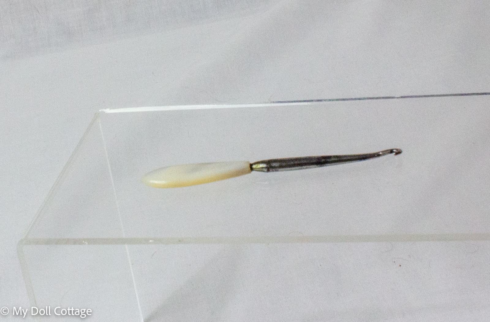 Victorian mother-of-pearl handled button hook displayed on a clear acrylic stand against a white background.