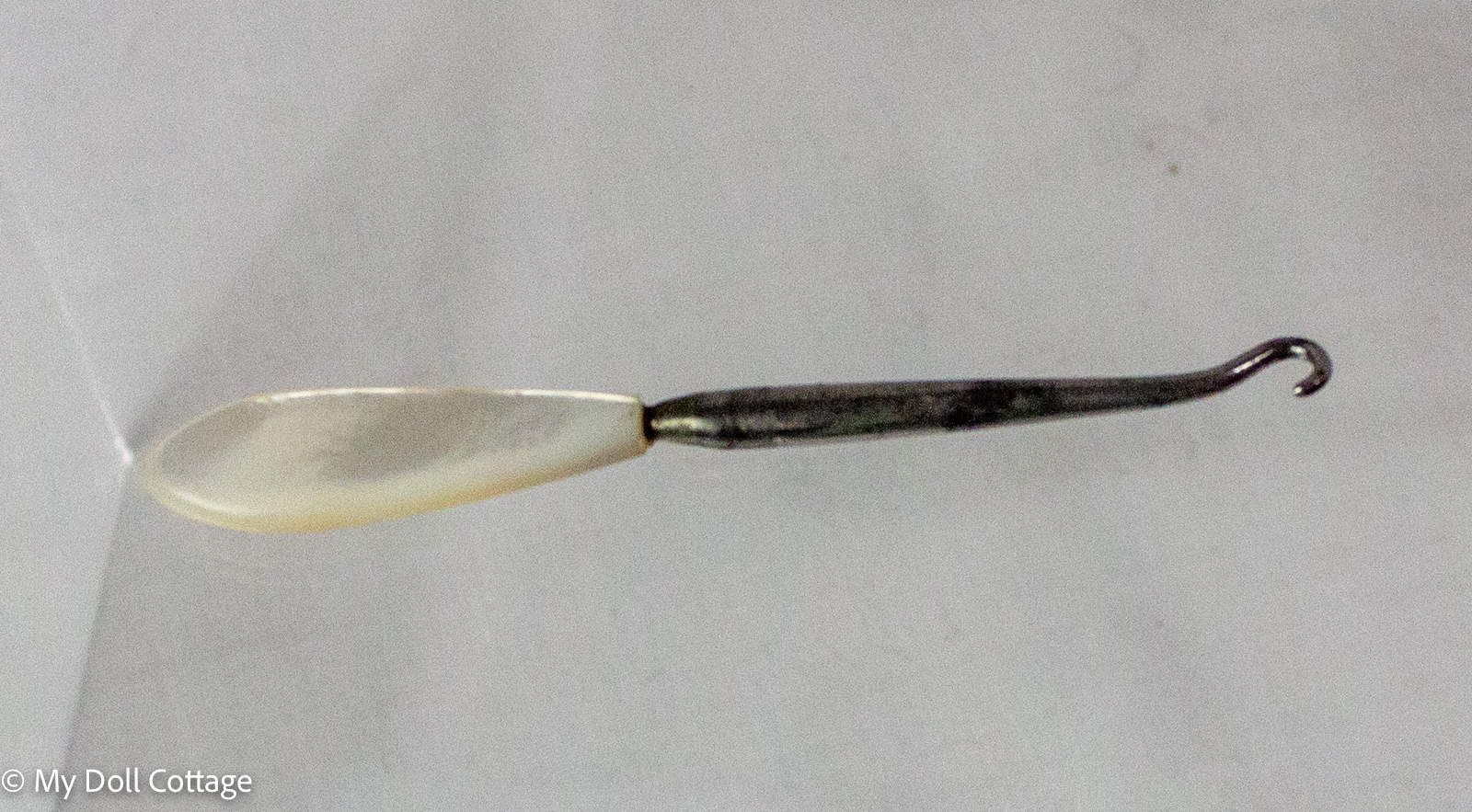 Victorian mother-of-pearl handled button hook displayed on a clear acrylic stand against a white background.