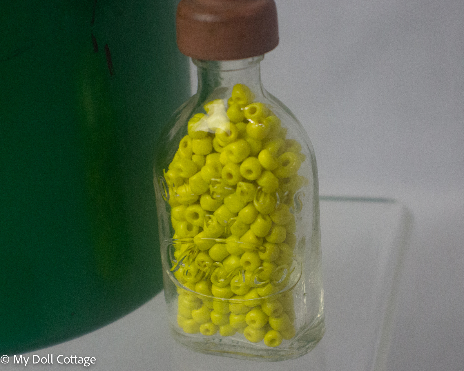 5. Close-up of miniature glass bottle filled with yellow beads beside green steriliser bucket.