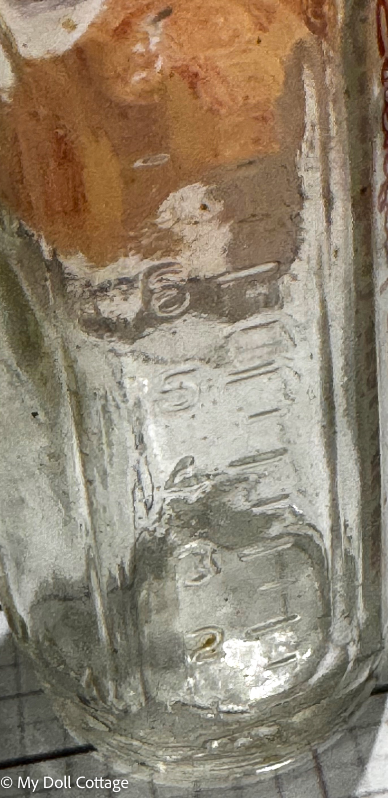 8. Close-up of embossed bottle measurements and maker markings on miniature glass bottle.