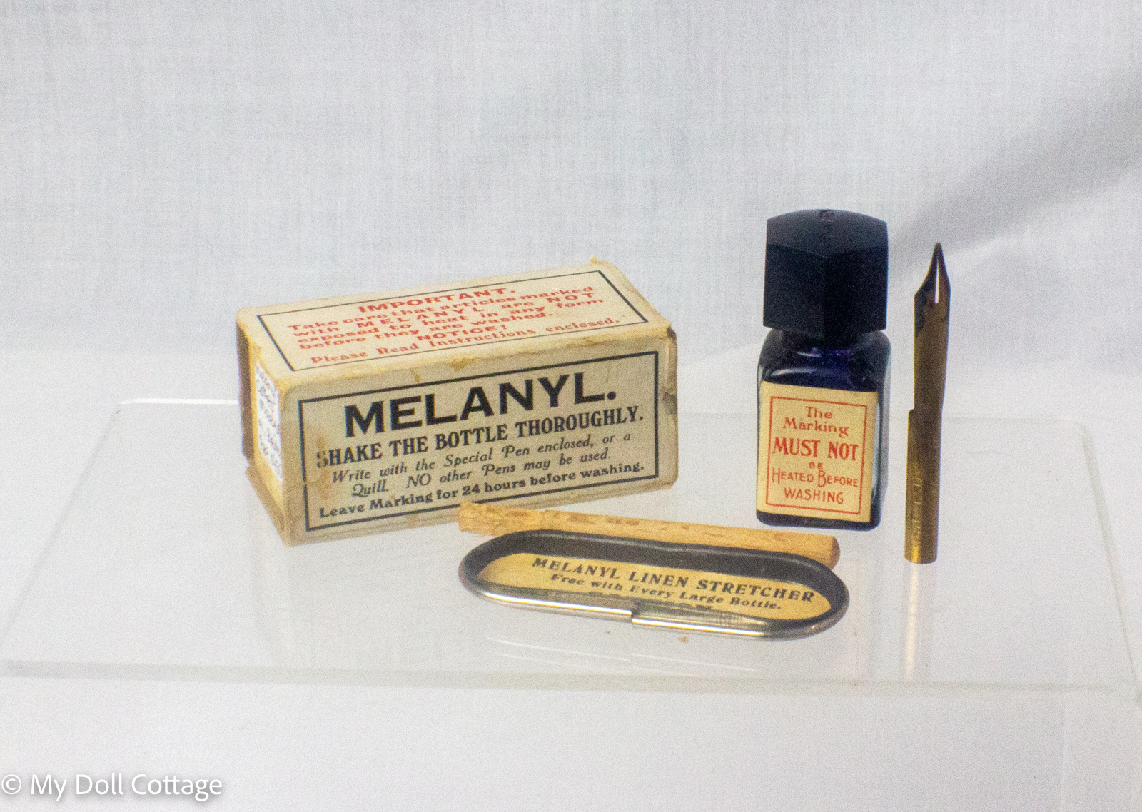 Vintage Melanyl indelible linen marking ink kit in original cardboard box with blue glass ink bottle, pen holder, steel nib and metal linen stretcher, manufactured in England. showing contents of packet