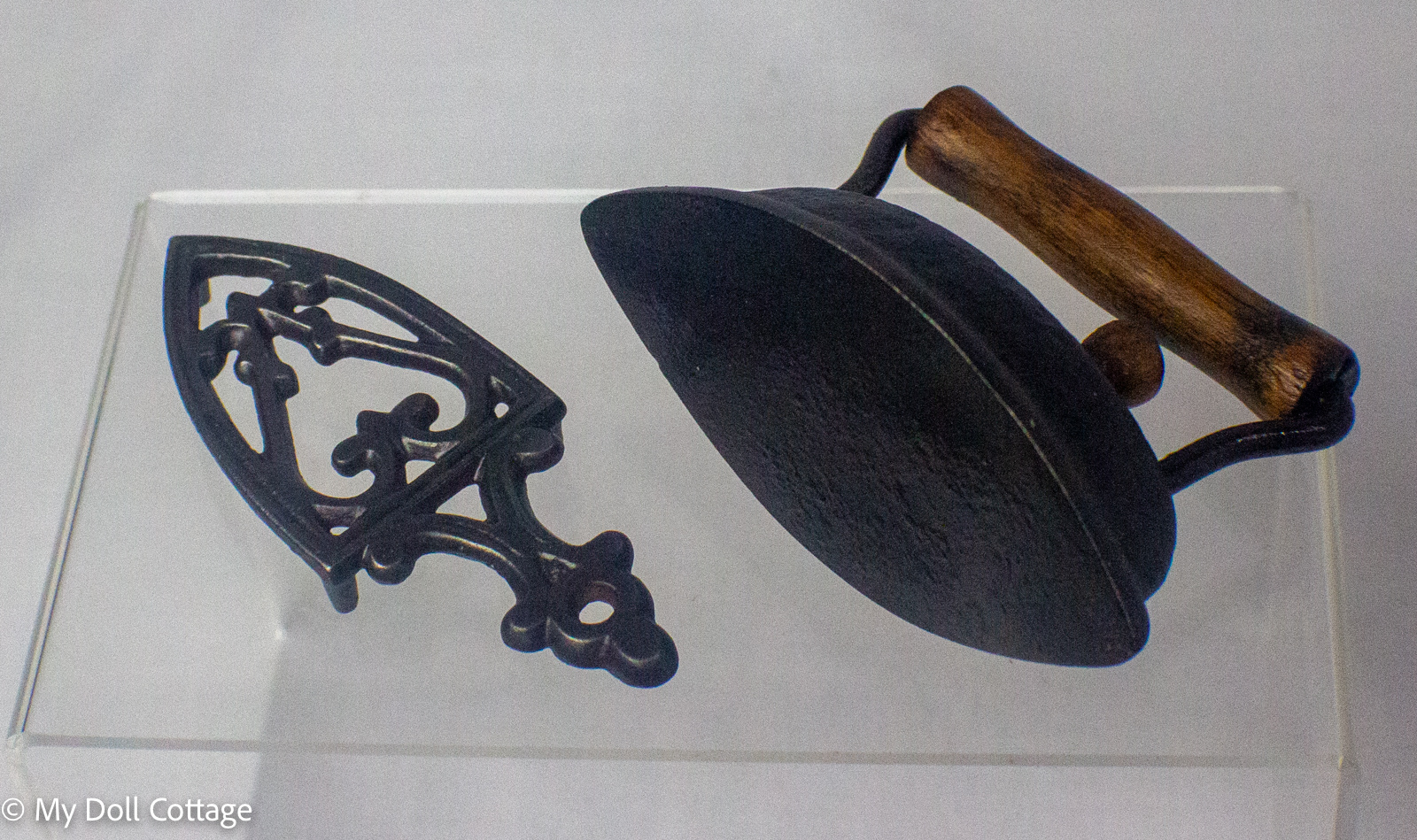 Angled view showing the miniature sad iron and matching ornate cast iron trivet.