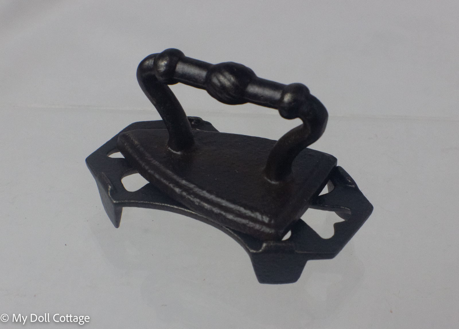 Side view of the iron removed from the stand, revealing the underside and hinged trivet construction. 