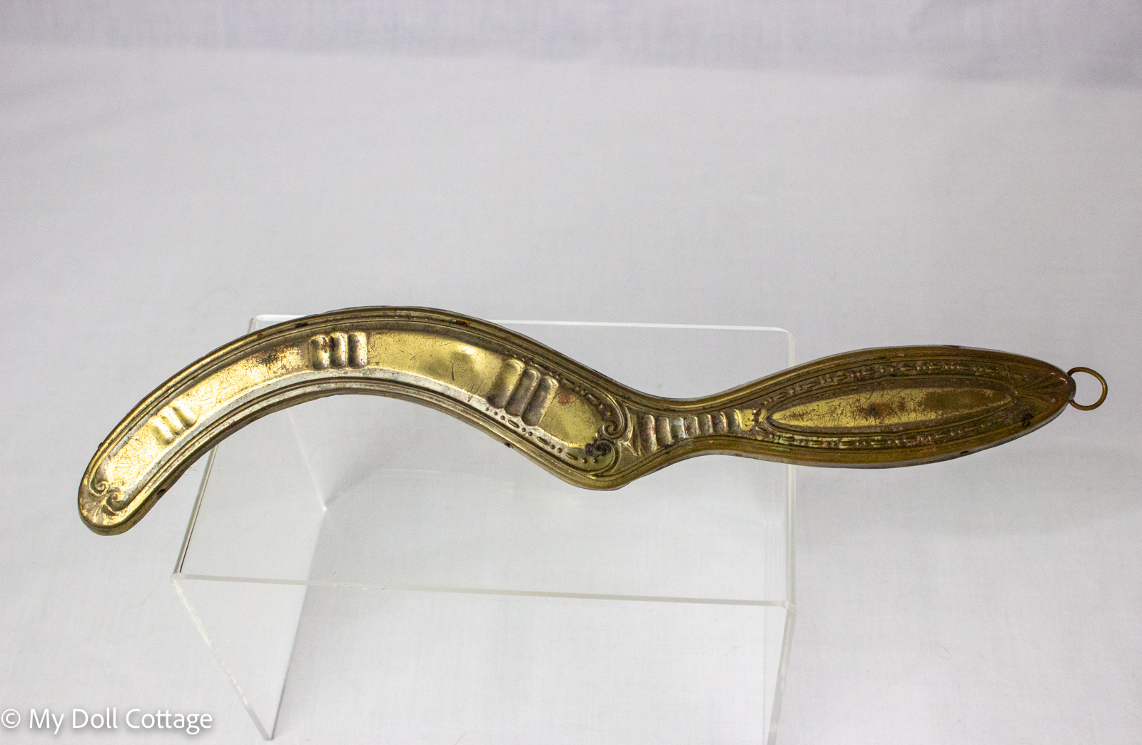 Decorative pressed-metal back of a c. 1890–1910 clothes brush showing its long curved handle, embossed ornamentation and metal hanging ring.