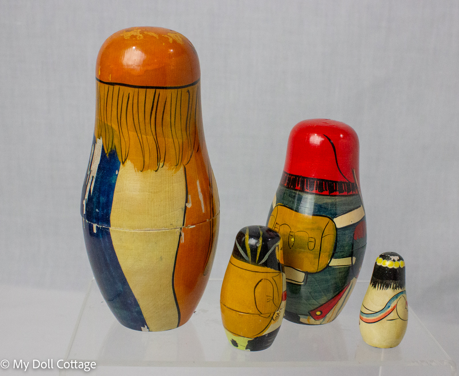 Alternate rear view of four graduated wooden matryoshka-style nesting dolls showing the painted clothing and worn finish.
