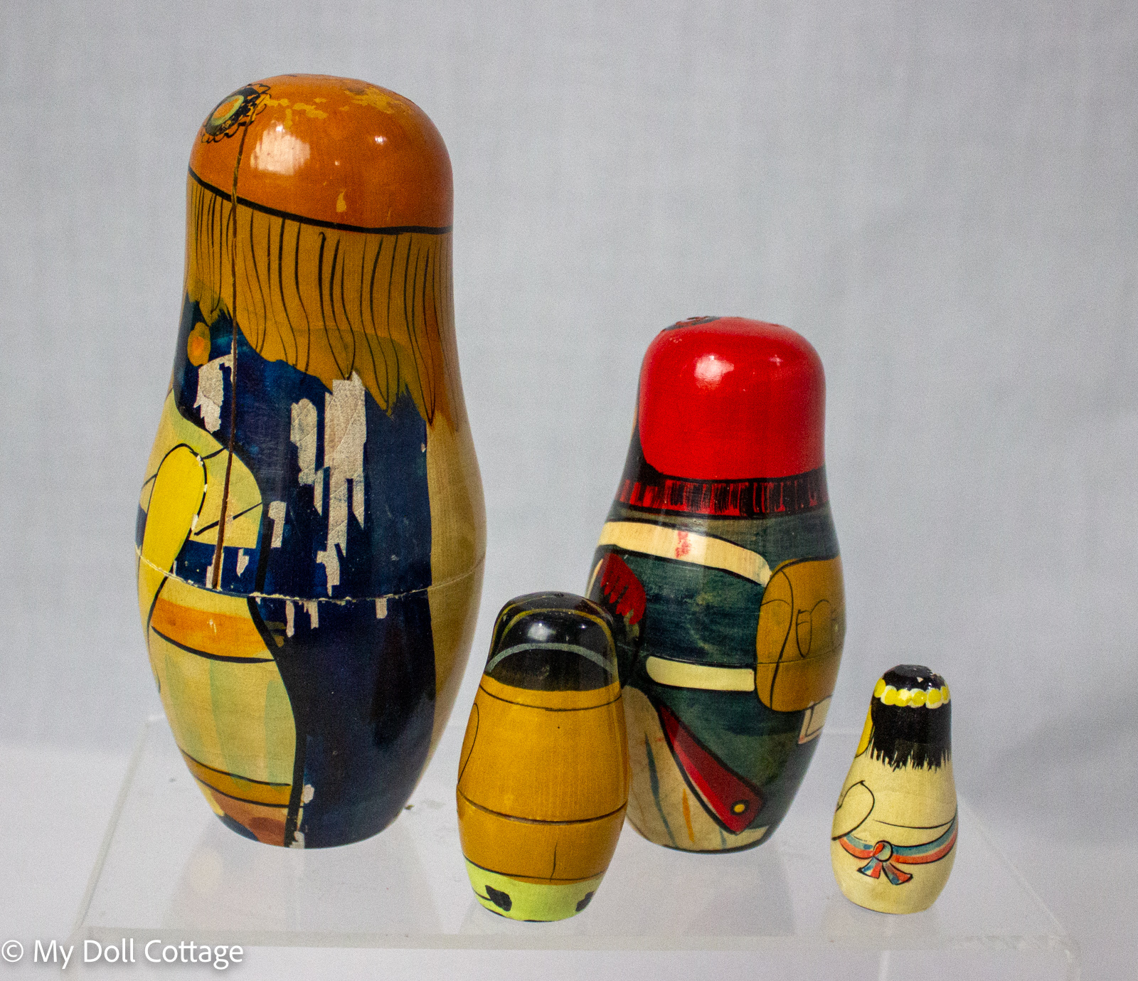 : Rear view of four vintage wooden nesting dolls showing painted costumes, surface wear and paint loss.