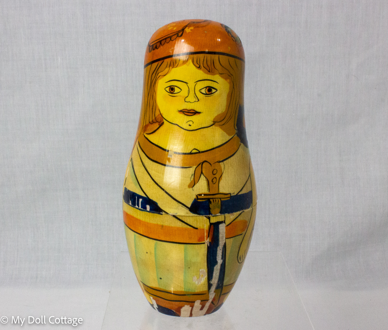 Front view of the largest vintage wooden nesting doll, painted with a long-haired historical character holding a sword.