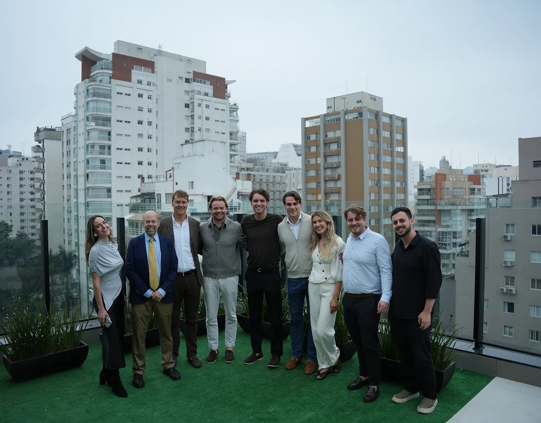 Group of nine people standing together on a rooftop terrace with city buildings in the background.