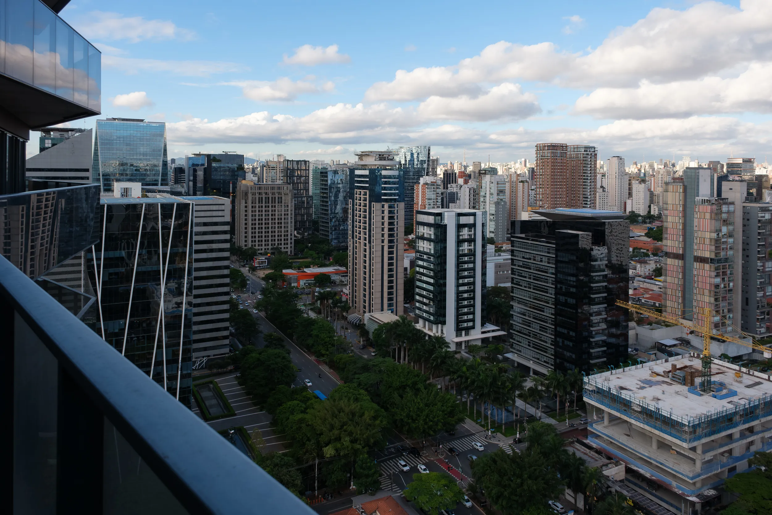 View of a modern cityscape with numerous high-rise buildings, a road with traffic below, and a partly cloudy sky.