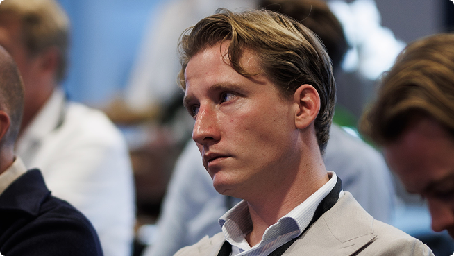 Een man met kort bruin haar en een baard die aandachtig luistert in een professionele setting.