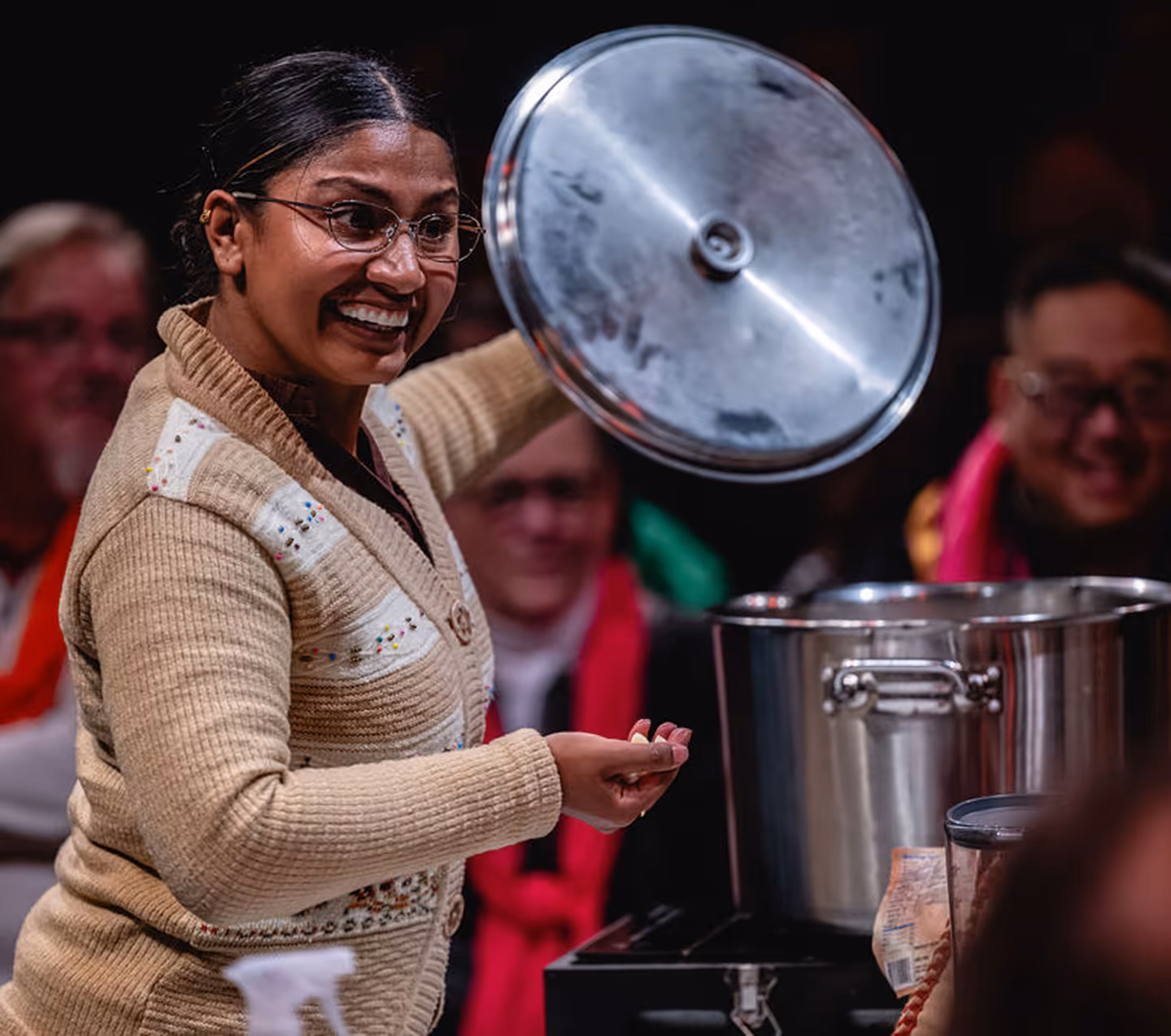 Smiling actor at Actors Theatre of Louisville lifts pot lid during immersive performance with audience.
