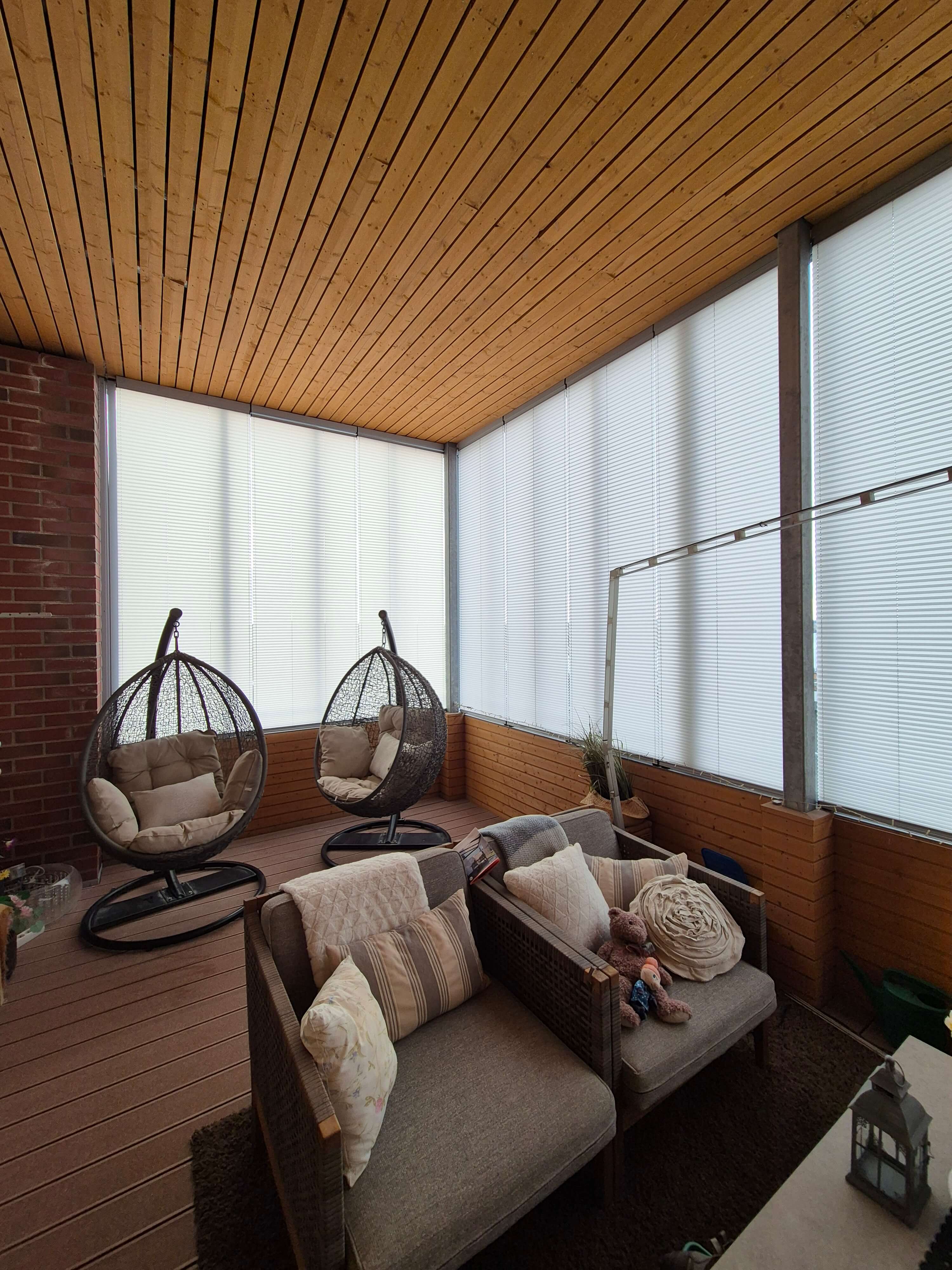 Suojattu terassi, jossa kaksi rottinkista keinutuolia ja kaksi nojatuolia tyynyillä ja pehmoeläimillä, valkoiset sälekaihtimet ikkunoissa ja puinen katto.