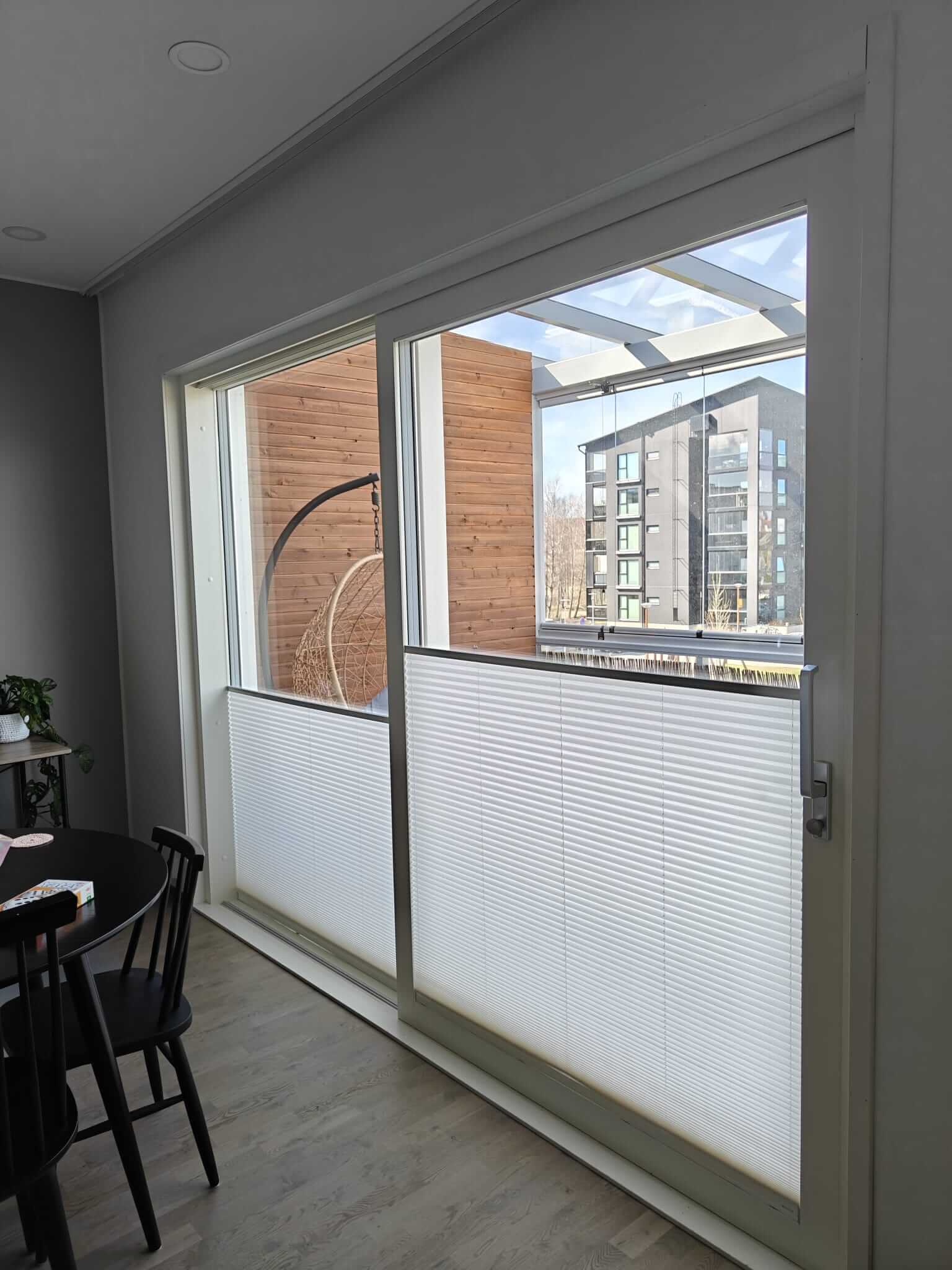 Isosta lasiovesta näkyy ulos parvekkeelle, jonka reunalla roikkuu punottu rottinkikeinu, ja taustalla näkyy kerrostalo.