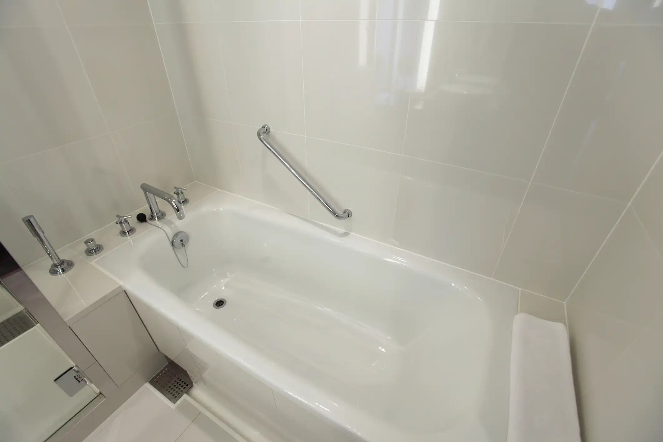 A clean, modern bathroom with a white bathtub, white tiled walls, and a silver grab bar.