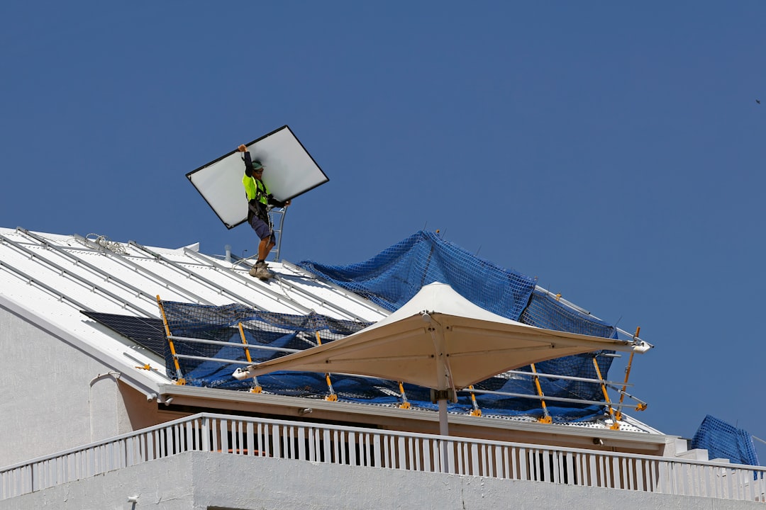 of a professional technician inspecting a solar collector on a roof - solar hot water repairs near me of a professional technician inspecting a solar collector on a roof - solar hot water repairs near me