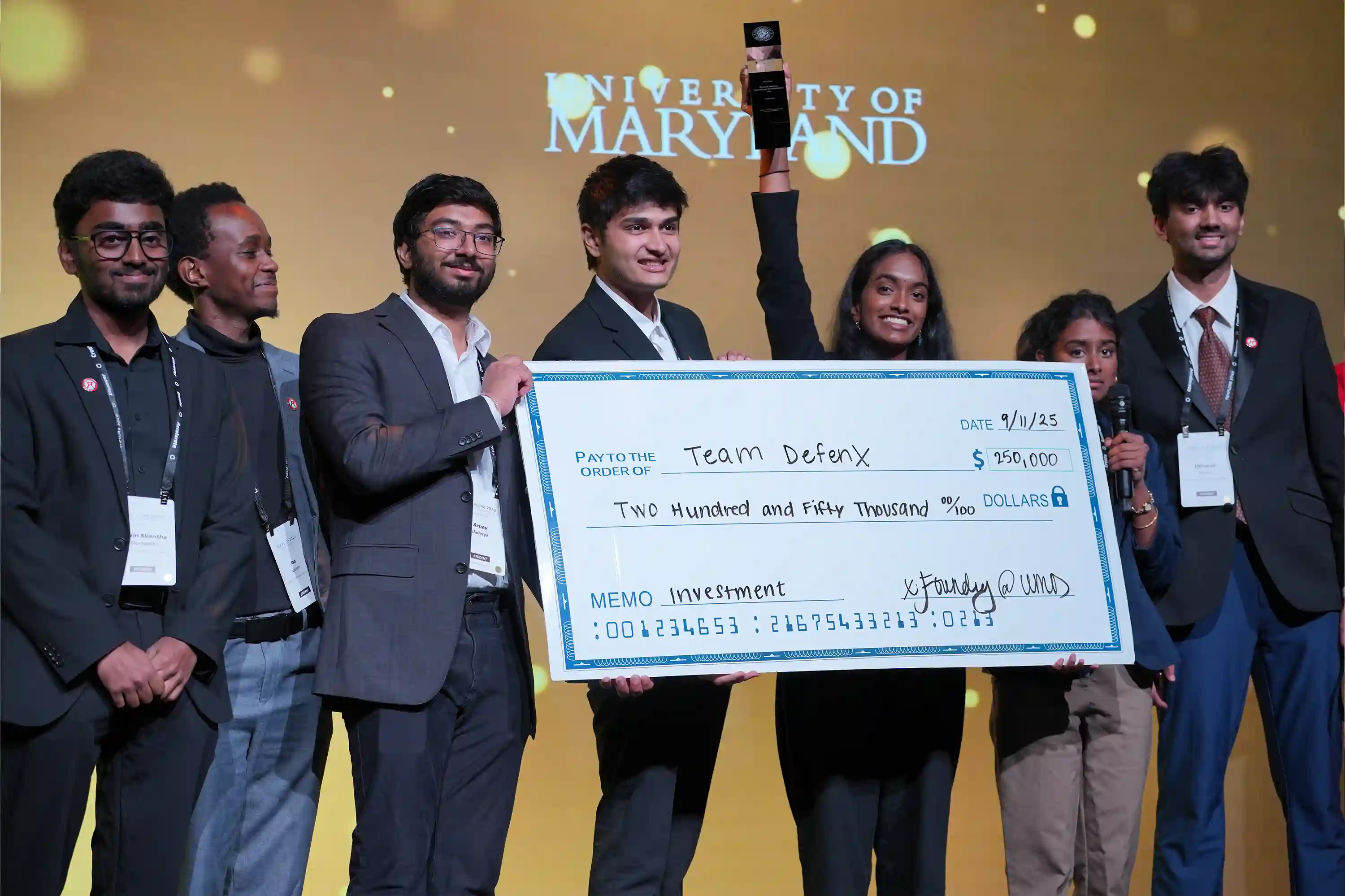Team DefenX holding $250,000 check and trophy on stage at University of Maryland event.