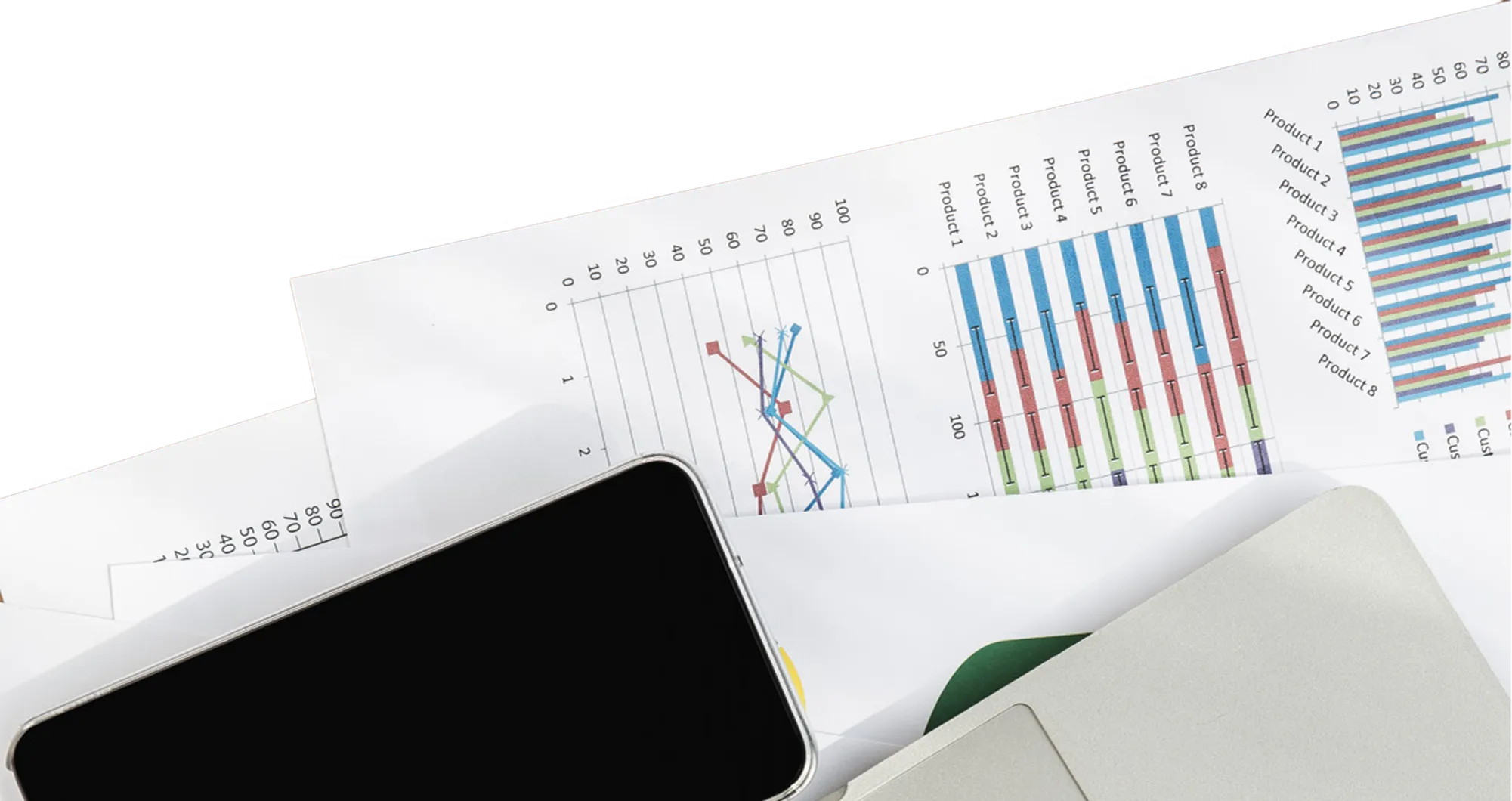 Top view of printed business charts and graphs partially covered by a smartphone and a laptop keyboard on a desk.