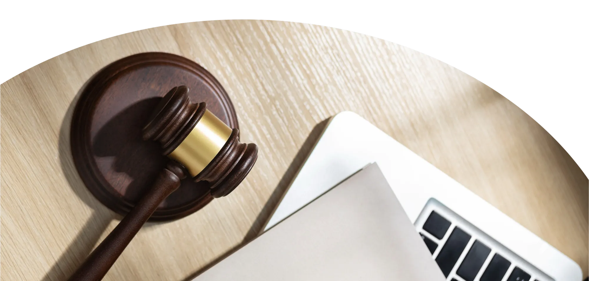 Wooden judge gavel with brass band resting on a wooden table next to a partially visible silver laptop and a folder.