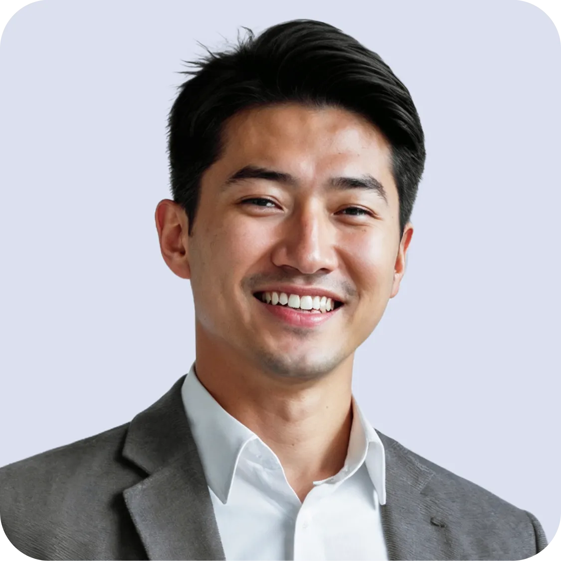 Smiling young Asian man with black hair wearing a gray suit jacket and white shirt against a light background.