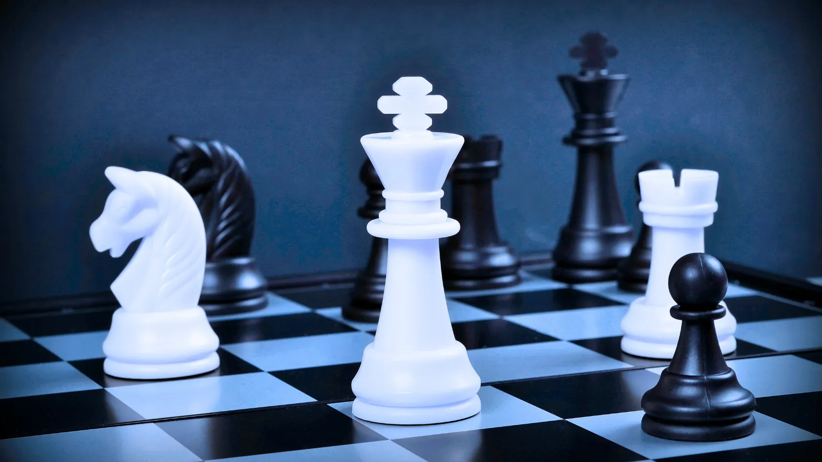Close-up of white and black chess pieces on a chessboard with white king prominently in the center.