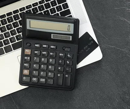 Black calculator displaying zero resting on a laptop keyboard with a black credit card partially visible.