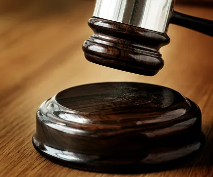 Close-up of a wooden judge's gavel striking a matching sound block on a wooden surface.