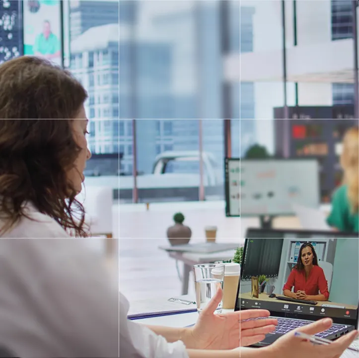 Woman participating in a video conference with another woman visible on a laptop screen in a modern office.
