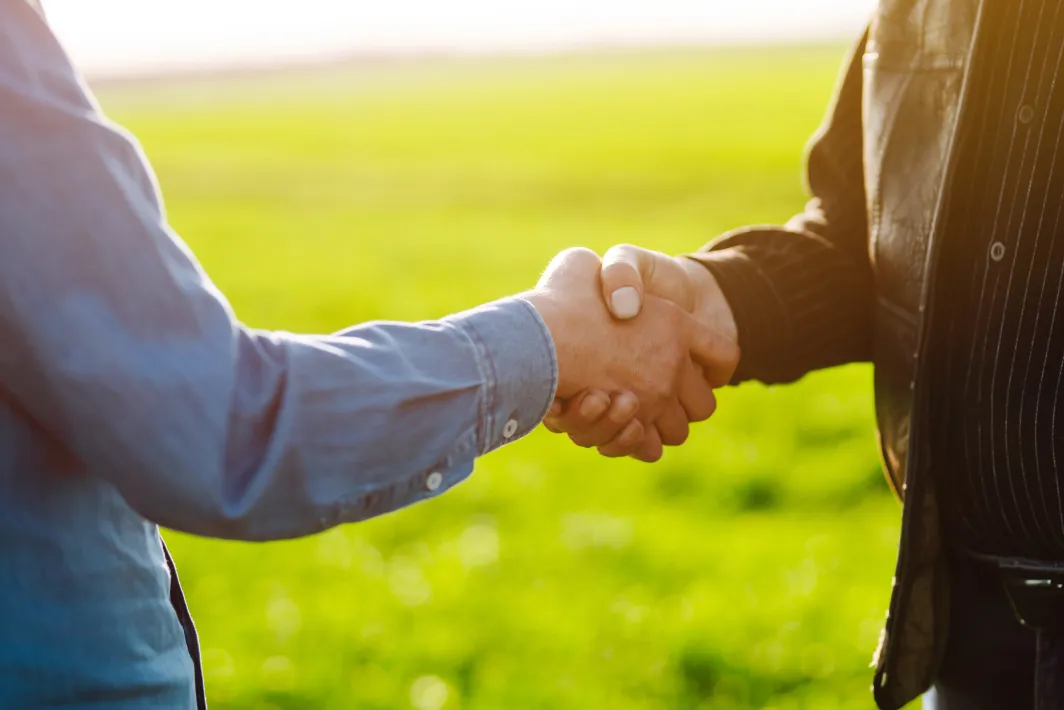Two people shaking hands while standing in a field