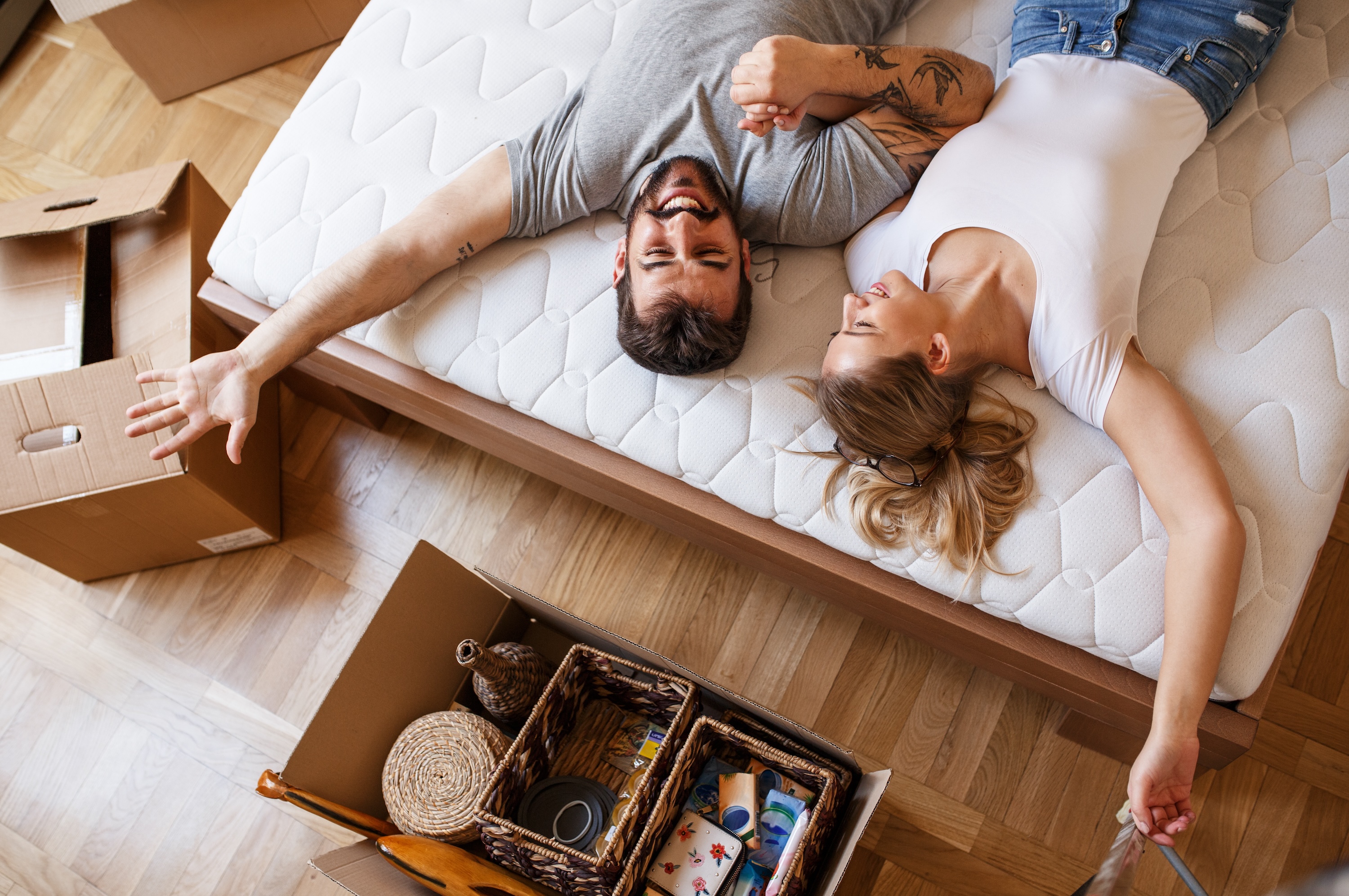 Happy couple lying on a new mattress on the floor surrounded by open moving boxes at The Grand at Riverside.