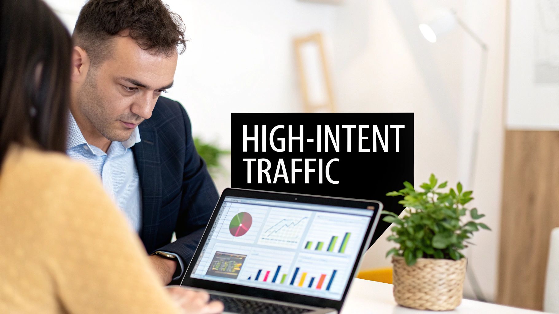 Two business professionals analyzing marketing data and charts on a laptop, discussing high-intent traffic.