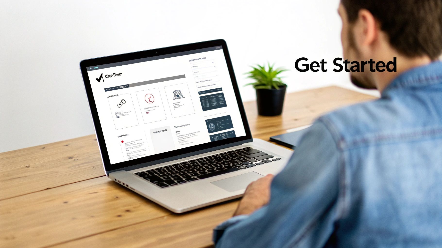 A person in a denim shirt views a laptop with a web interface on a wooden desk.