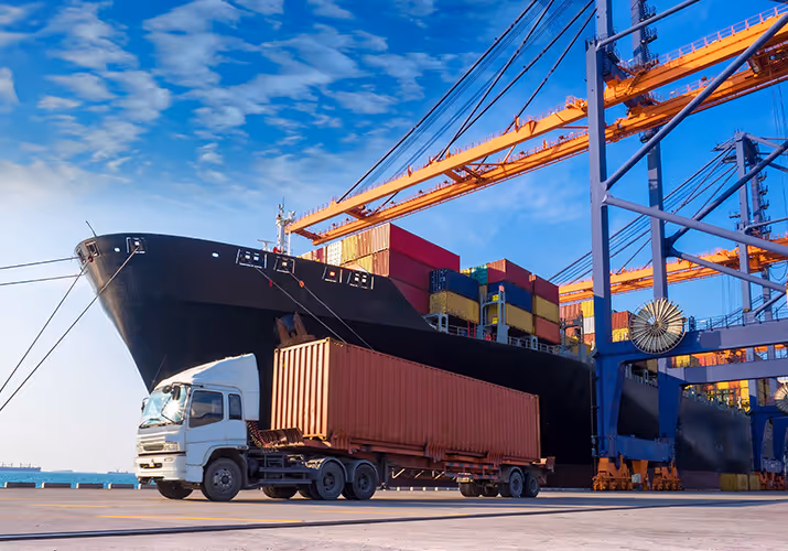 Cargo truck in forefront with a large cargo ship behind it unloading in the port.