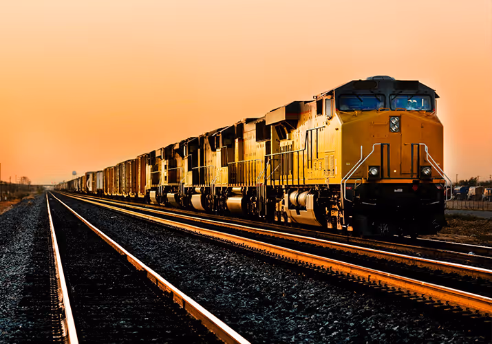 Train moving along railroad tracks at sunset.