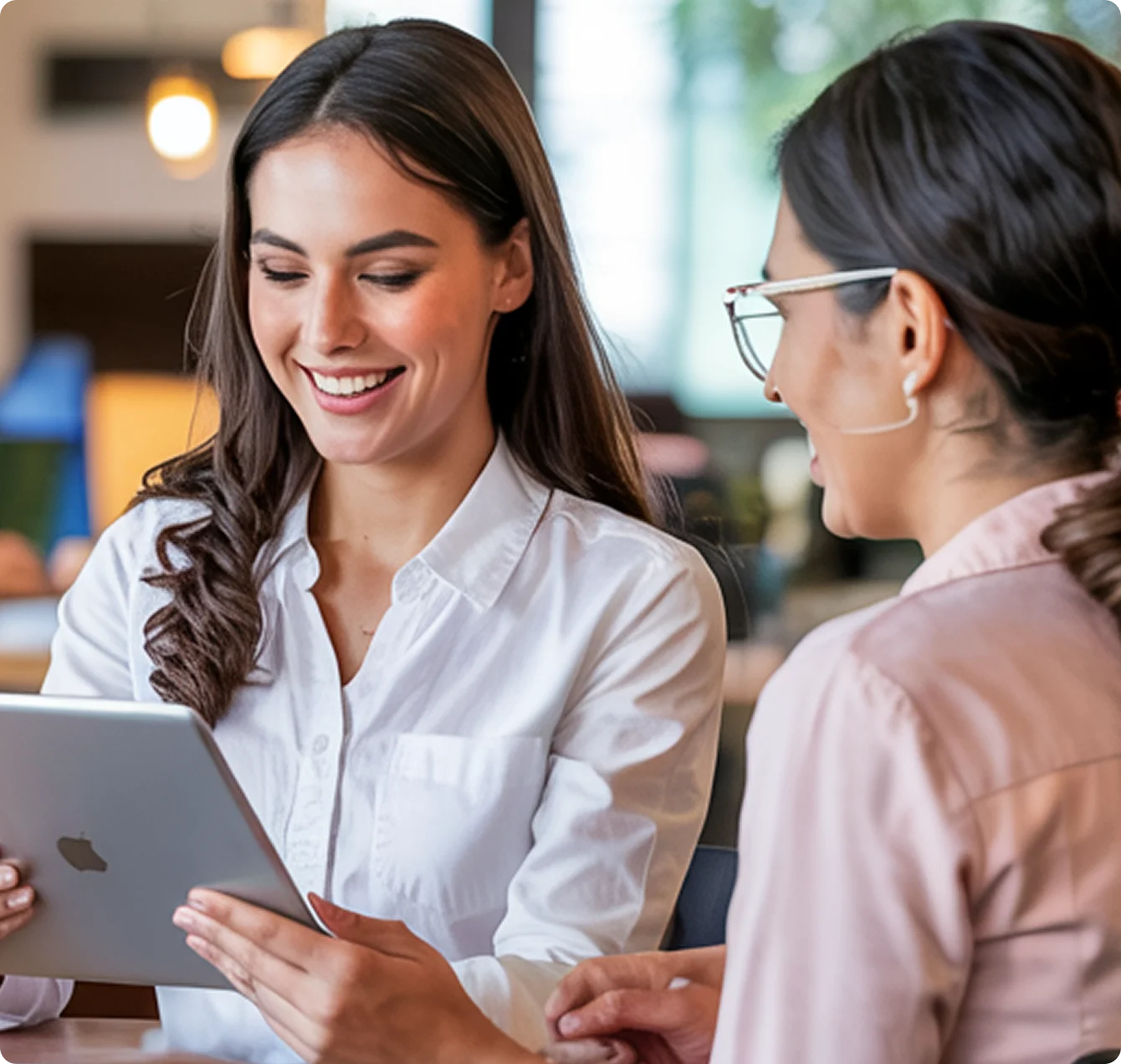 Two women smiling and looking at a tablet together in a modern indoor setting.