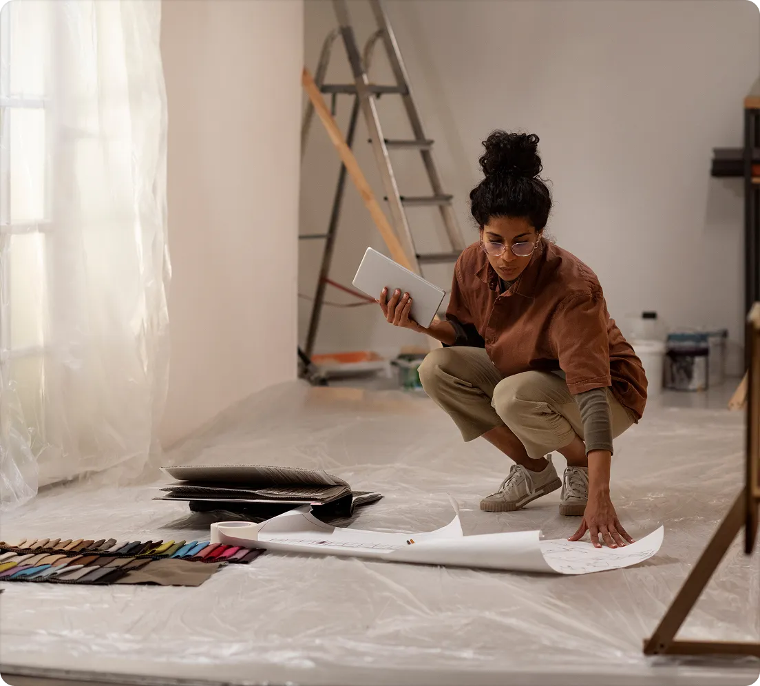 A woman kneeling on a dust sheet while renovating a stripped-back room