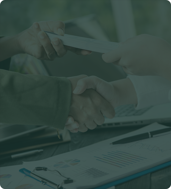 Two people shaking hands over a desk with financial charts, a pen, and a laptop, symbolizing approval and funding.