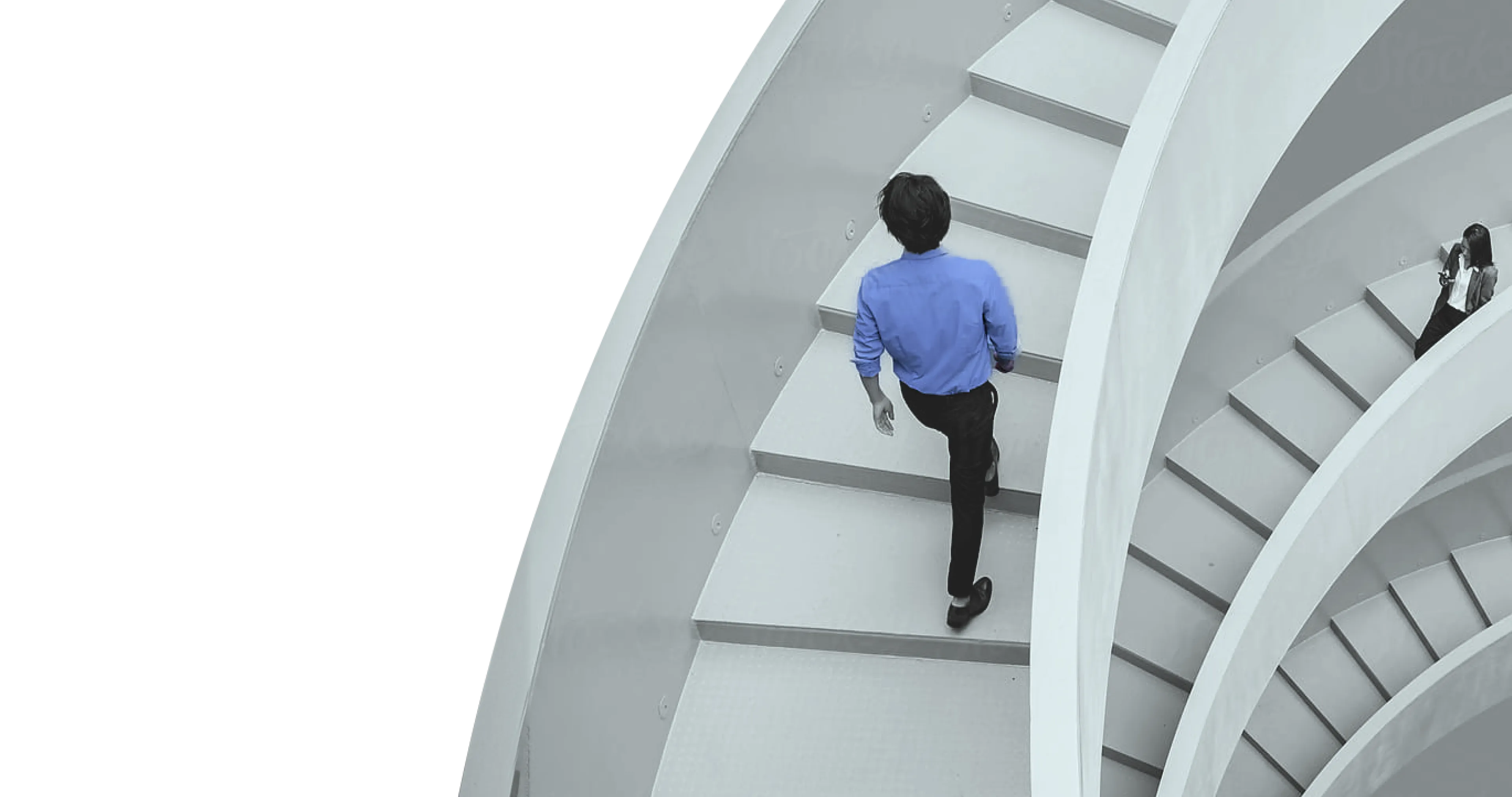 Wide angle photo of a man in a blue shirt walking up a winding white staircase