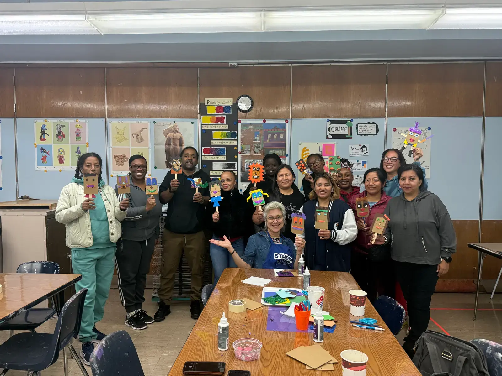 Group of adults displaying colorful paper craft puppets in classroom