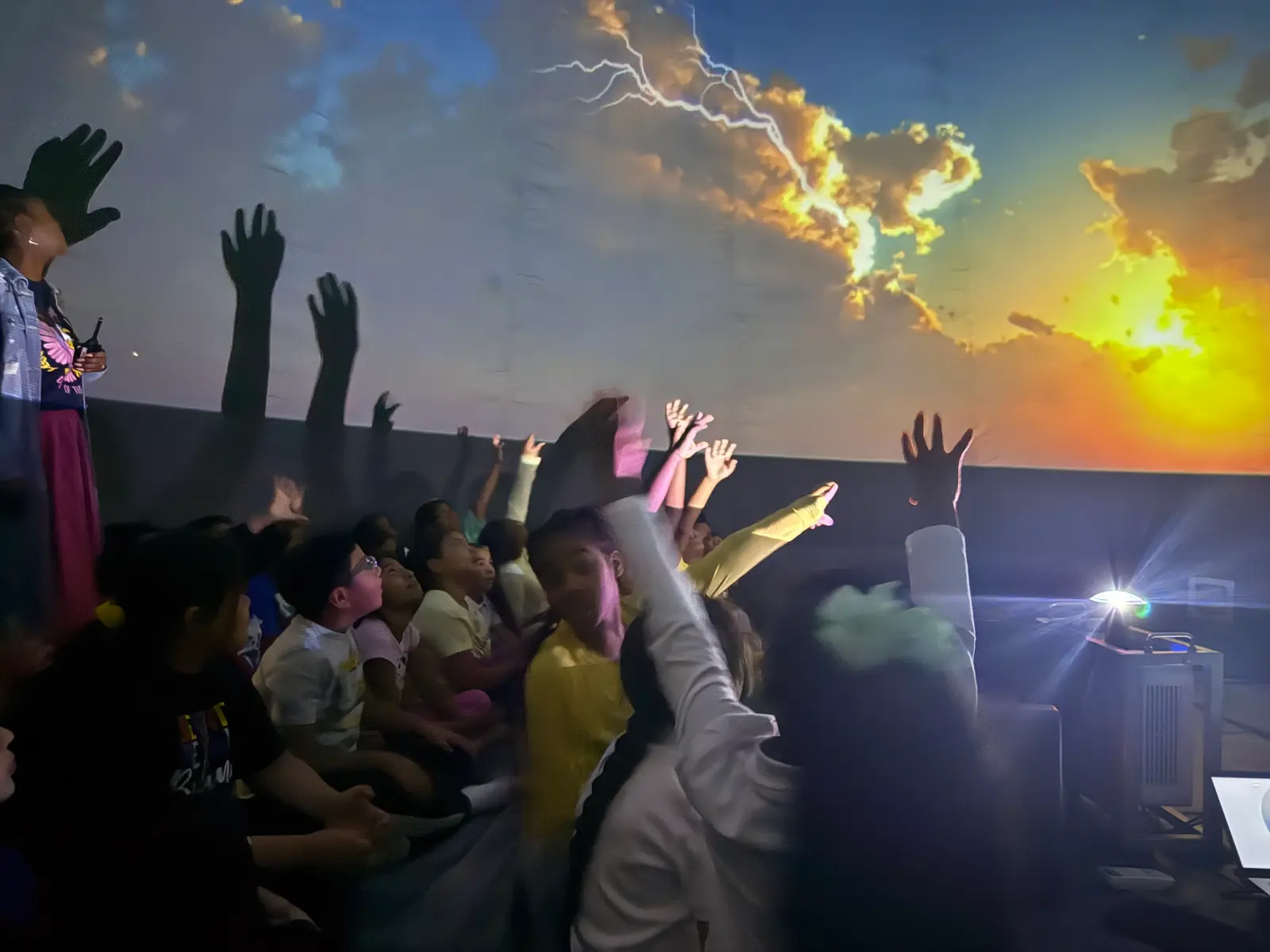 Students raising hands during planetarium demonstration with projected sky