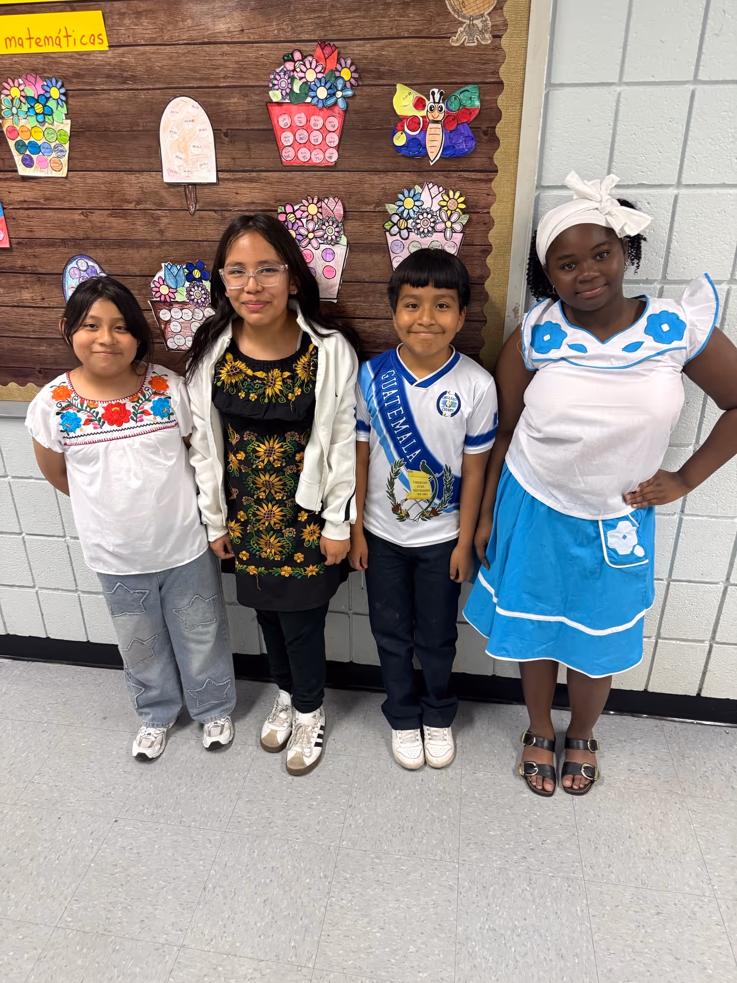 Four students in Guatemalan cultural attire pose in classroom hallway