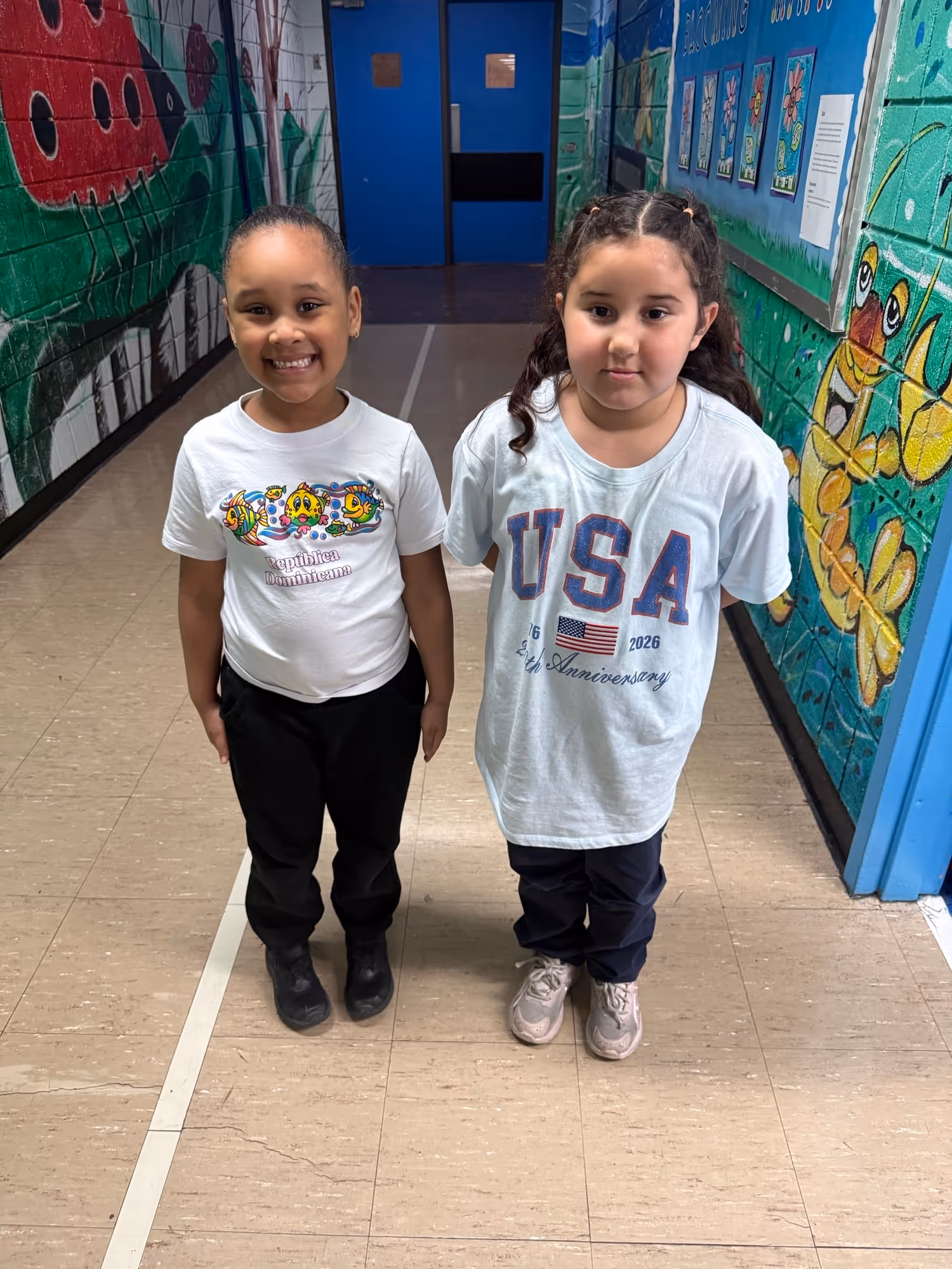 Two elementary students posing in school hallway with colorful murals